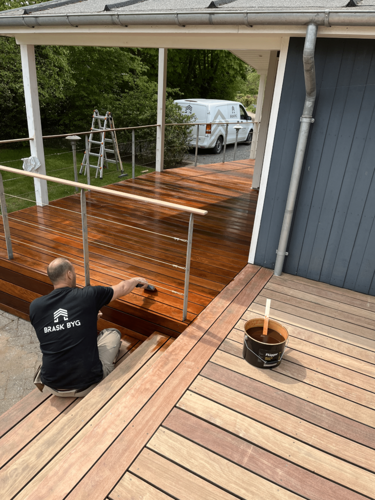 Håndværker olierer nyt trædæk ved hus
